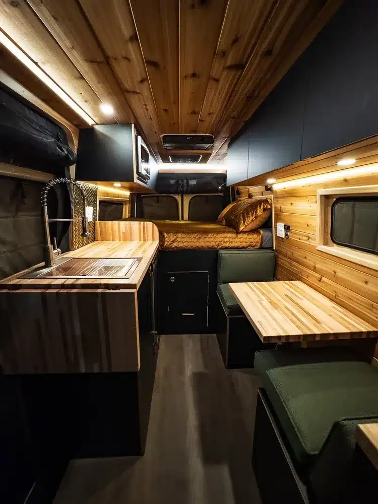 Innenraum eines modern ausgebauten Kastenwagen-Campervans mit Holzausbau, Sitzgruppe und Küchenbereich