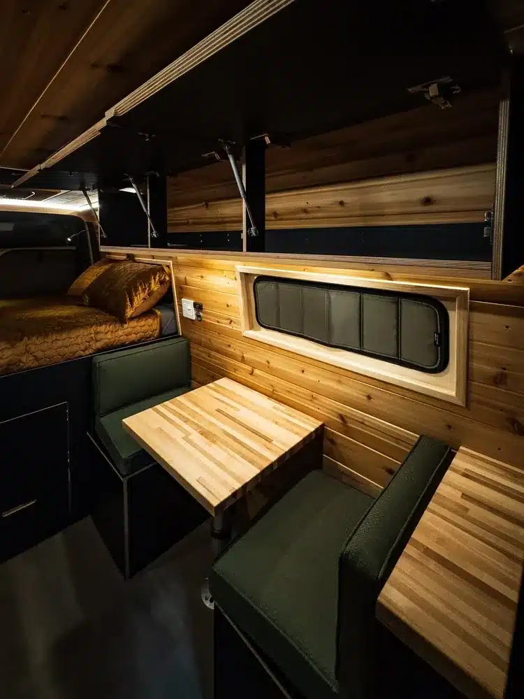 Innenraum eines ausgebauten Mercedes-Benz Sprinter Campervans mit Sitzgruppe, Tisch und Holzverkleidung