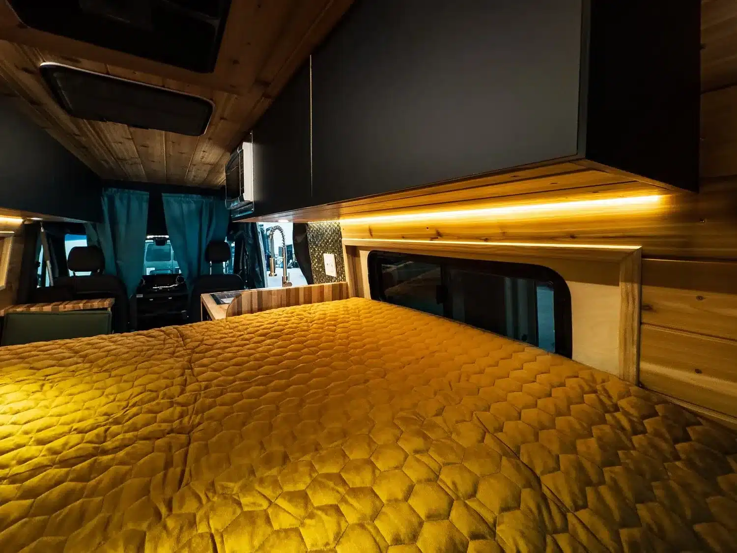 Innenraum eines ausgebauten Mercedes-Benz Sprinter 144” High Roof Campervans mit Bett, Schränken und Holzverkleidung