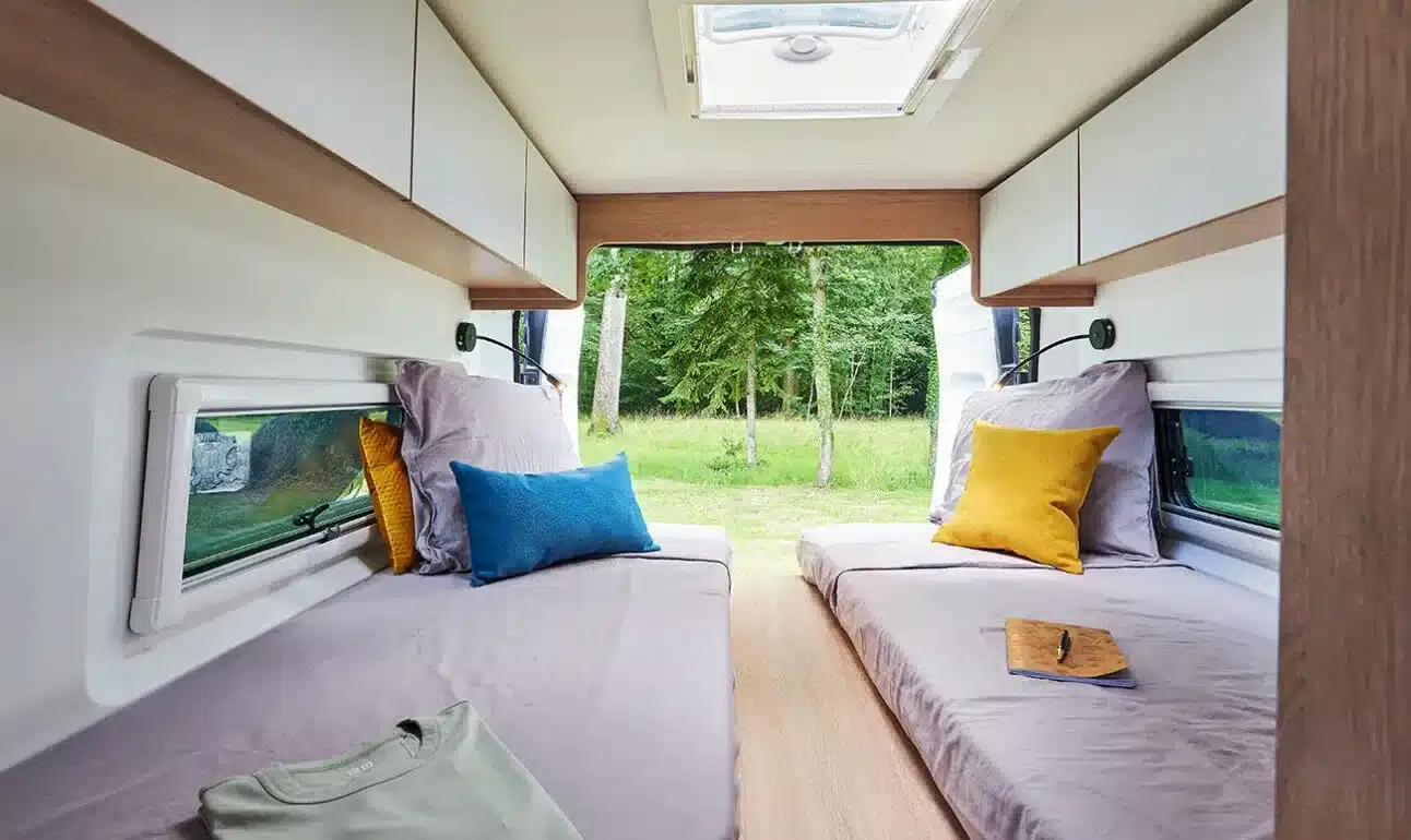 Innenansicht des Schlafbereichs im Joa Camp Kastenwagen 63T mit zwei Einzelbetten, Oberschränken und Blick nach draußen