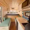 Moderner, hell gestalteter Innenraum eines kompakten Campervans JOLENE mit Schlafbereich, Küchenzeile und Sitzbank.