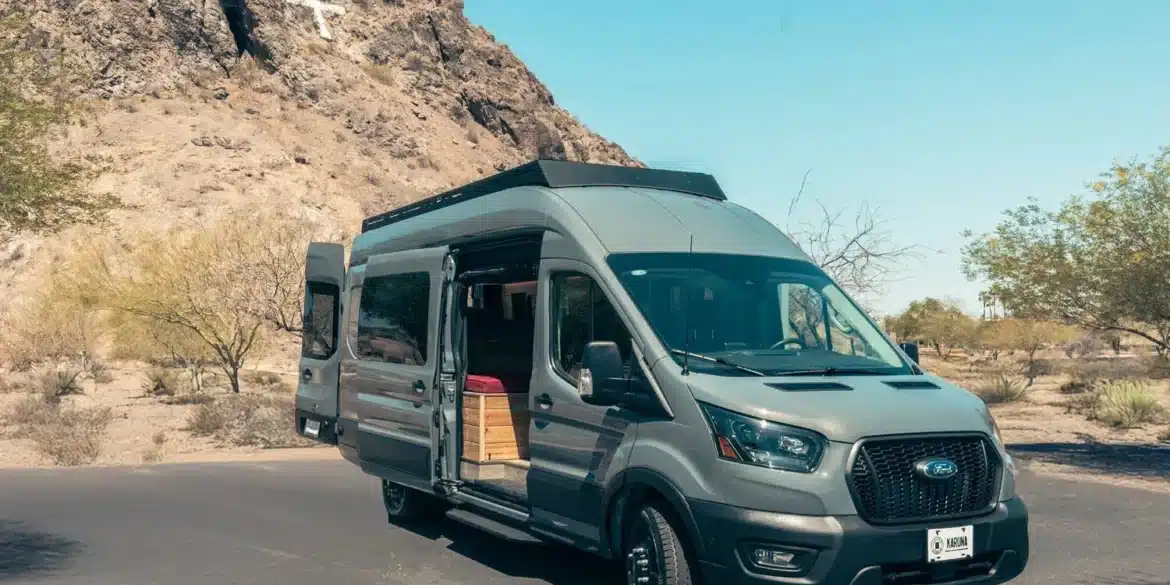 KARUNA Ford Transit Campervan mit geöffneten Türen, geparkt vor felsiger Landschaft unter blauem Himmel.