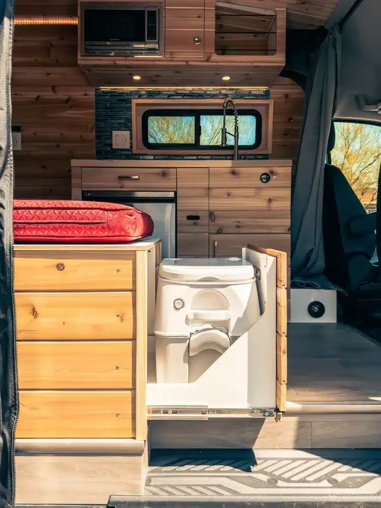 Innenraum eines Campervans mit Holzausbau, Küchenzeile, Kühlschrank, Mikrowelle und ausziehbarer Kassettentoilette