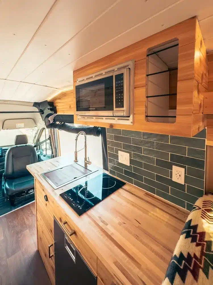 Moderner Küchenblock im Lonely Cactus 2 Campervan mit Induktionskochfeld, Mikrowelle, Spüle und Holzarbeitsplatte.