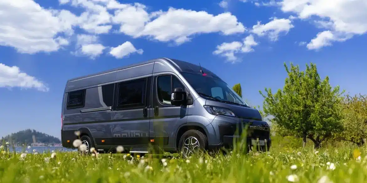 Malibu Relax Kastenwagen geparkt auf einer grünen Wiese unter blauem Himmel mit weißen Wolken.