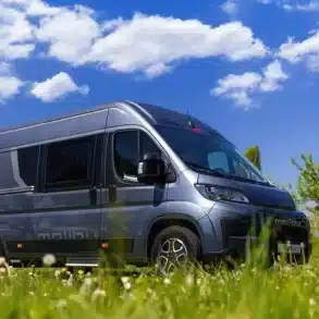 Malibu Relax Kastenwagen geparkt auf einer grünen Wiese unter blauem Himmel mit weißen Wolken.