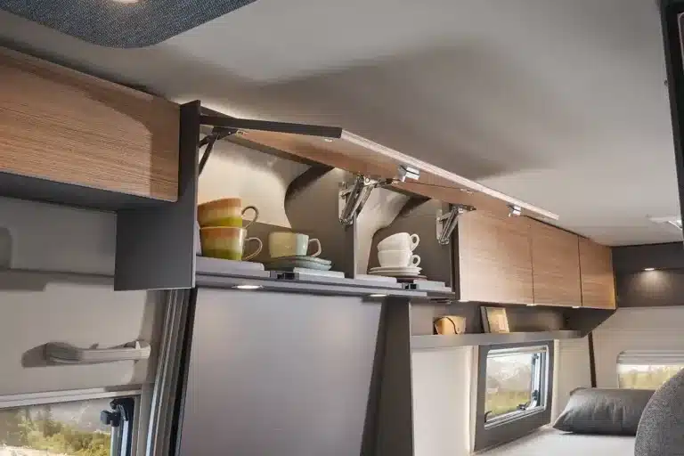 Oberhalb einer Sitz- oder Liegefläche geöffnete, grifflose Hängeschränke im Malibu Relax Kastenwagen mit Geschirr darin.