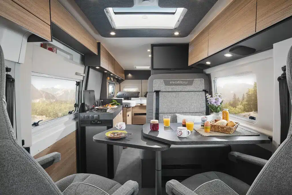 Innenansicht des Malibu Relax Kastenwagens mit modernem Wohnbereich, Tisch, Sitzgruppe und Blick zur Heckbetten.