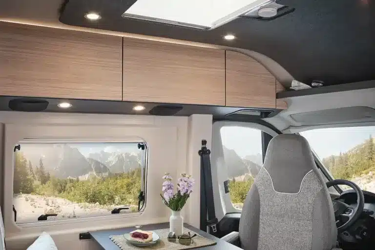 Innenansicht des Malibu Relax Kastenwagens mit Tisch, grauen Sitzen und modernen Hängeschränken.