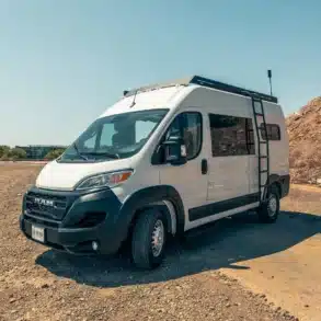 Malvan Ram Promaster 136 High Roof Kastenwagen mit Dachträger und Leiter auf staubigem Untergrund in der Sonne.