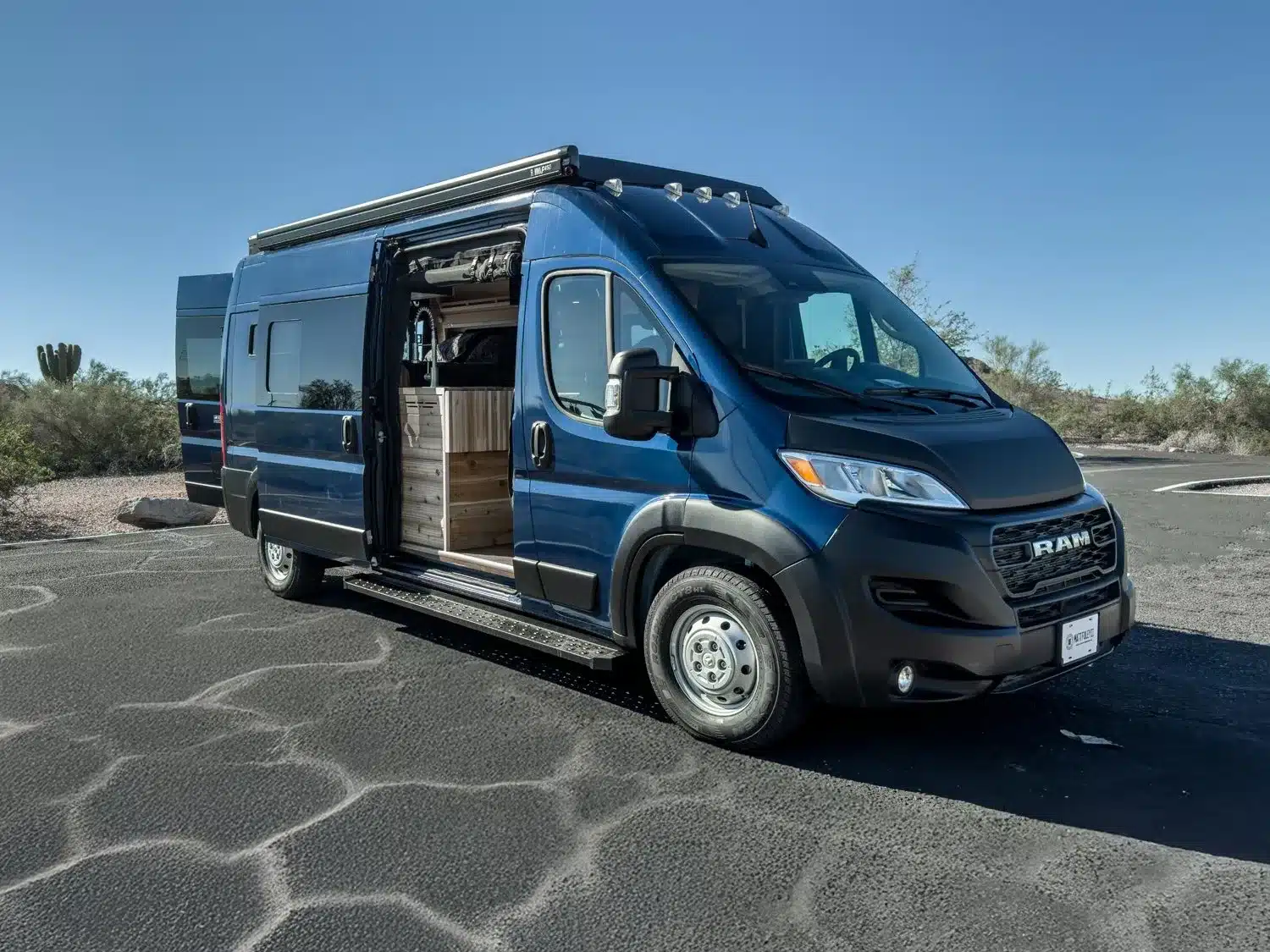 Blauer Matt Foley II Campervan, RAM Promaster 2500 High Roof, steht im Freien mit offenem Innenraum.