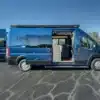 Seitenansicht eines blauen Matt Foley II Campervans mit geöffneten Türen und sichtbarem Innenausbau.