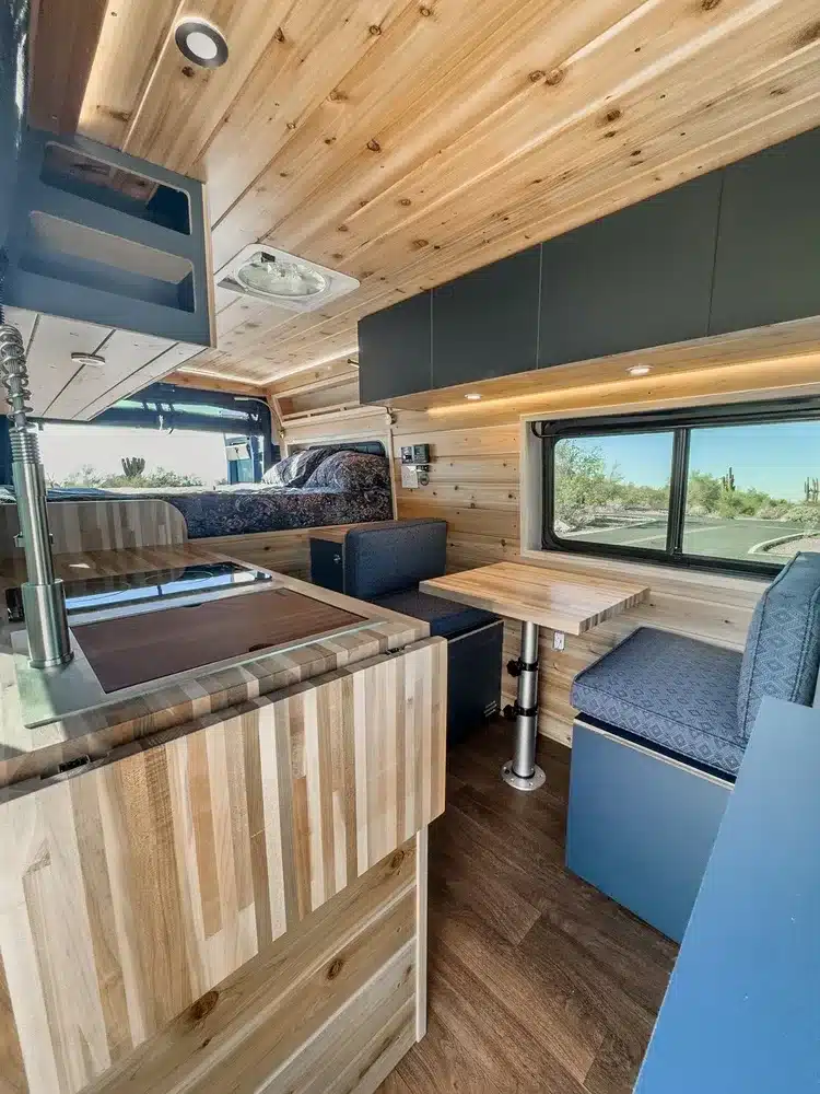 Innenansicht eines Matt Foley II Campervans mit Holzverkleidung, Küchenzeile, Sitzbank, Tisch und Schlafbereich.