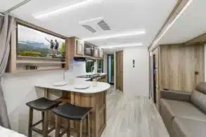 Innenansicht eines MPG 2400PD Travel-Trailers mit Küche, Essbereich, Sofa und hellen Holzmöbeln.