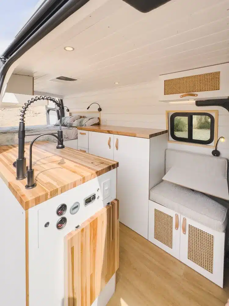 Innenraum eines individuell ausgebauten Mercedes-Benz Sprinter 144 mit Massivholz-Arbeitsplatten, weißen Möbeln, Sitzgelegenheit und modernem Wohnambiente.