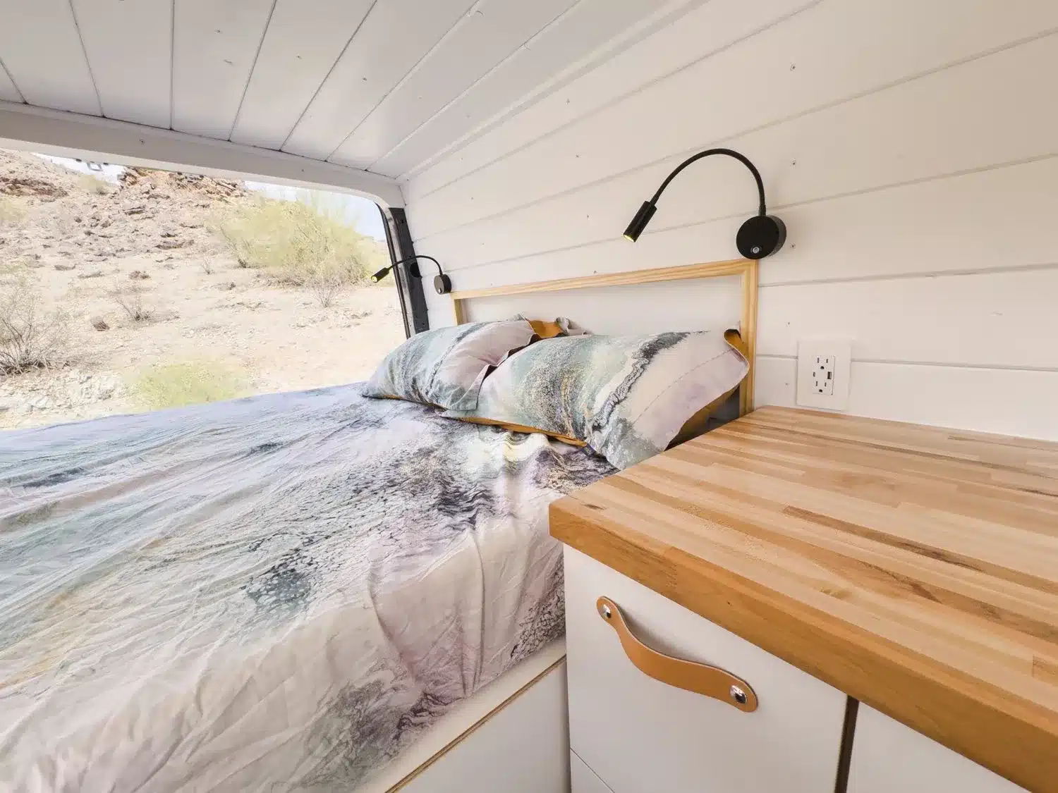 Heller Innenraum eines individuell ausgebauten Mercedes-Benz Sprinter 144 Kastenwagens mit Bett, Leselampe und Massivholz-Arbeitsfläche.