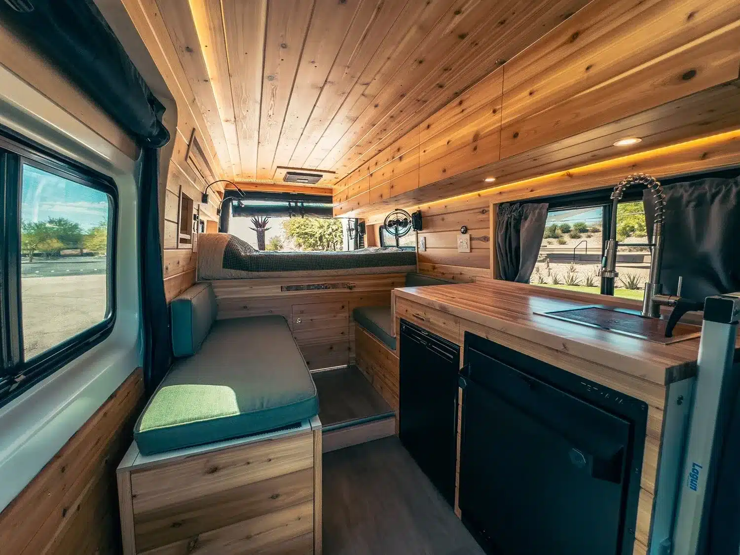 Innenraum des Sage Campervan mit Holzausbau, Sofa, Küchenzeile und großen Fenstern.