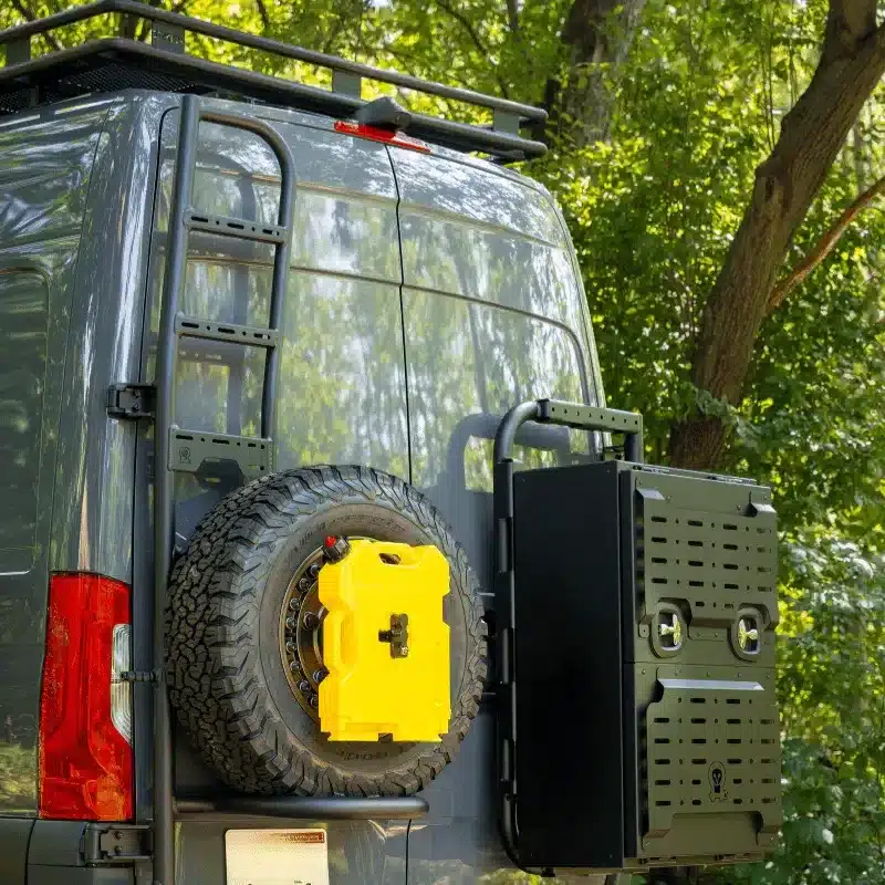 Heck eines Mercedes Sprinter Campervans mit Leiter, Reserverad und Zubehör vor Bäumen