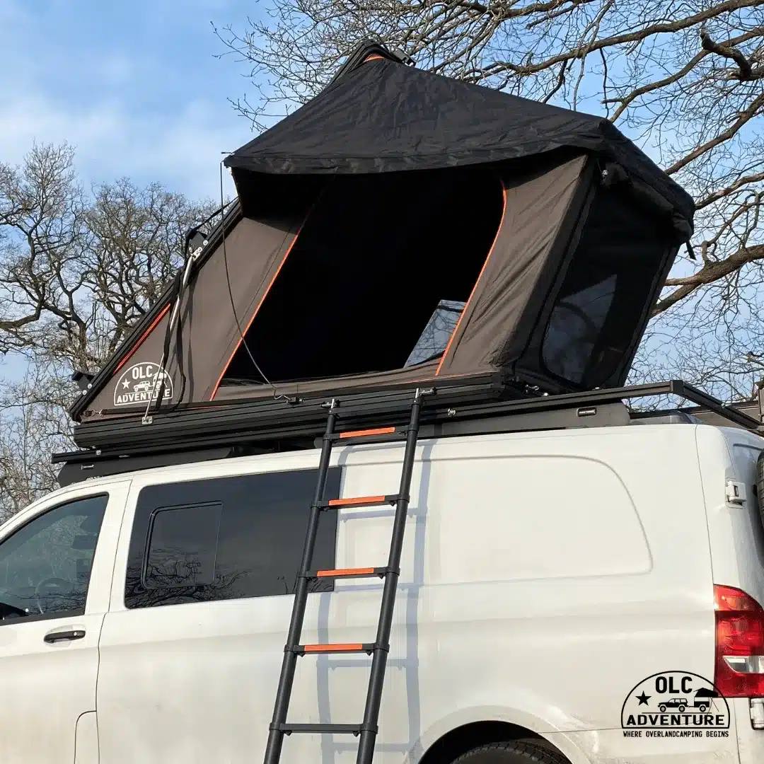 Geöffnetes OLC140ALU 2.0 Dachzelt mit Erker auf einem weißen Kastenwagen und ausgefahrener Teleskopleiter, im Freien geparkt.