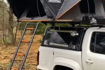 Hartschalen-Dachzelt OLC150Alu Hybrid von OLC Adventure auf einem Pickup mit aufgebauter Teleskopleiter im Wald.