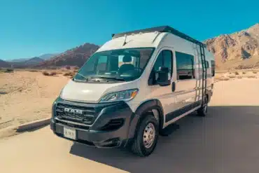 RAM Promaster 2500 Campervan mit Hochdach und Solaranlage in einer sonnigen Wüstenumgebung vor Bergen.