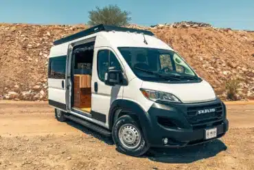 Weißer Ram Promaster 2500 High Roof Campervan mit geöffneter Seitentür, abgestellt auf einer Schotterpiste vor einer steinigen Böschung