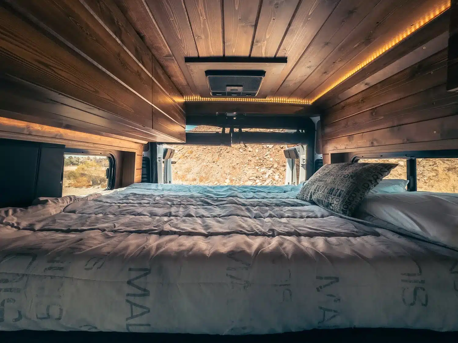 Blick auf das fest installierte Bett mit Bettwäsche und Holzdecke im ausgebauten Ram Promaster 2500 High Roof Van