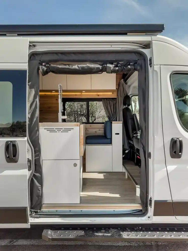 Seitliche Schiebetür eines Ram Promaster Kastenwagens mit sichtbarem Camper-Innenausbau, Sitzgruppe und Küche