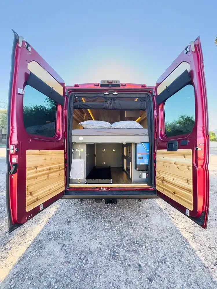 Geöffnete Hecktüren des Red Rover Vans, dahinter komfortabler Innenausbau mit Bett und Stauraum für Vanlife.