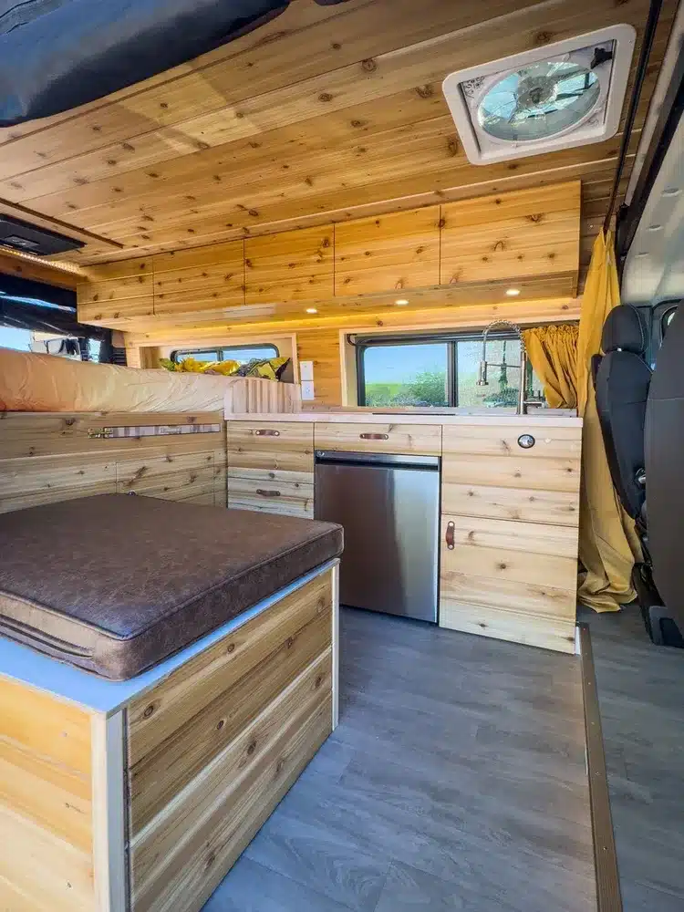 Innenraum des River Song RAM Promaster 136 Kastenwagens mit Holzverkleidung, Sofa-Zone, Küche und Kompressorkühlschrank