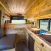 Hochwertig ausgebauter Innenraum eines River Song RAM Promaster 136" High Roof, mit Holzverkleidung, Küchenzeile, Sofa-Zone und großer Liegefläche.