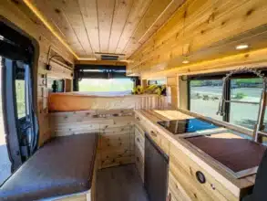Hochwertig ausgebauter Innenraum eines River Song RAM Promaster 136" High Roof, mit Holzverkleidung, Küchenzeile, Sofa-Zone und großer Liegefläche.