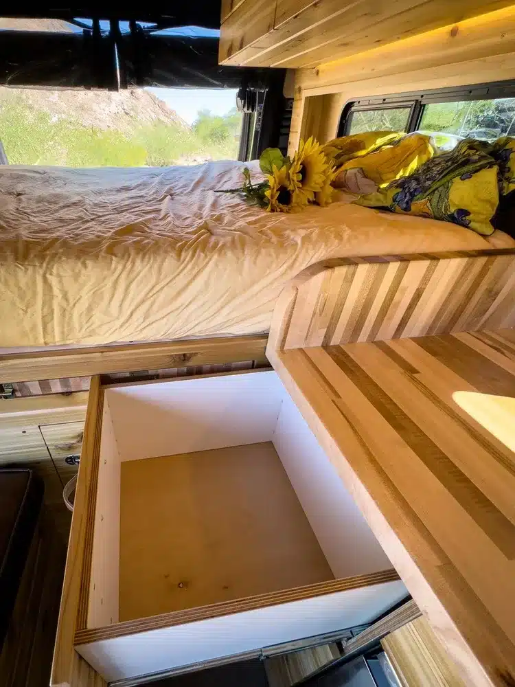 Innenansicht eines Campervans mit ausziehbarem Butcher-Block-Tisch, Stauraum und Liegefläche im River Song RAM Promaster 136
