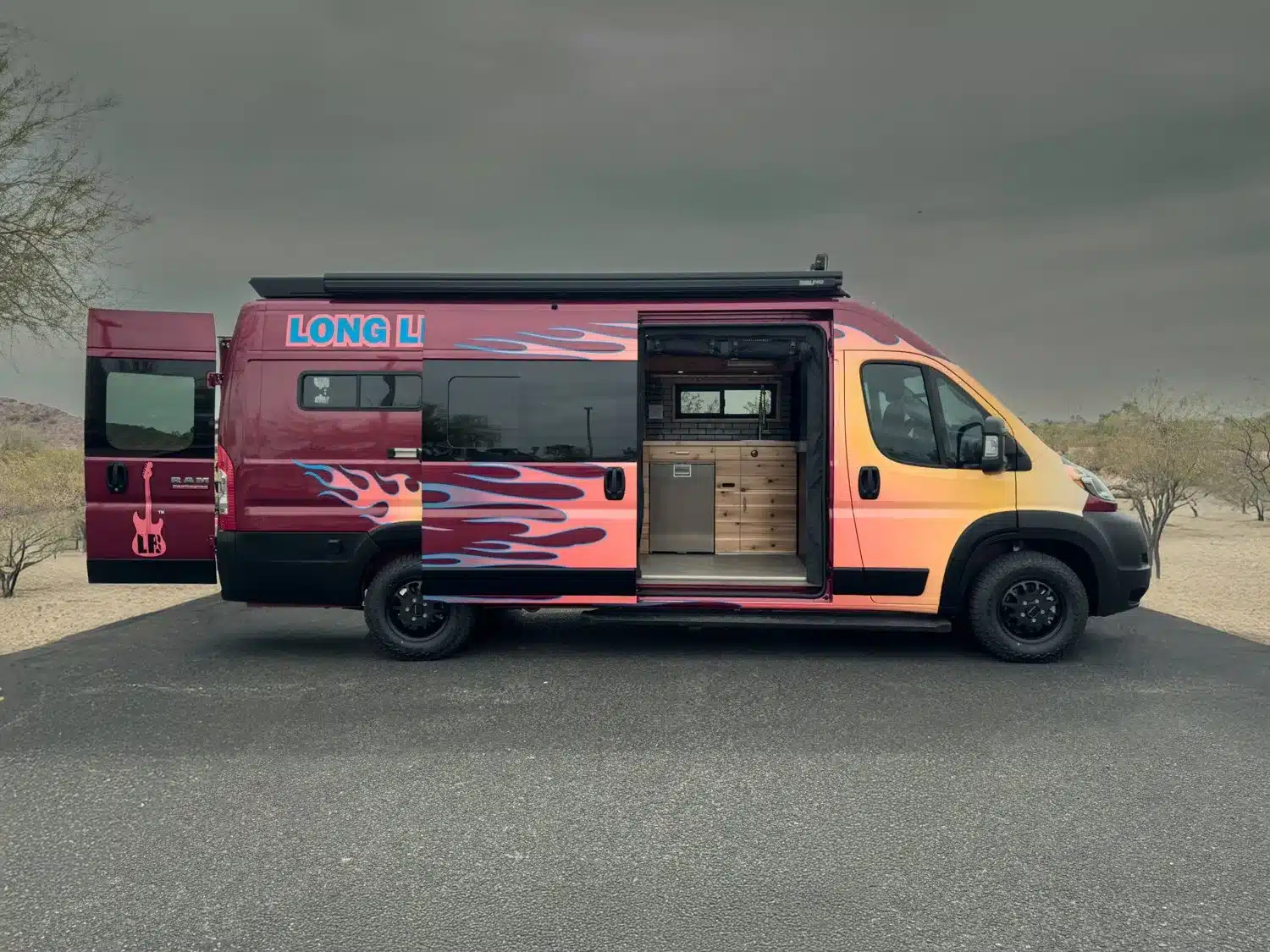 Seitenansicht eines Boho Sapho Campervans auf RAM Promaster 3500 Basis mit offener Schiebetür und Sicht auf Küchenmodul.