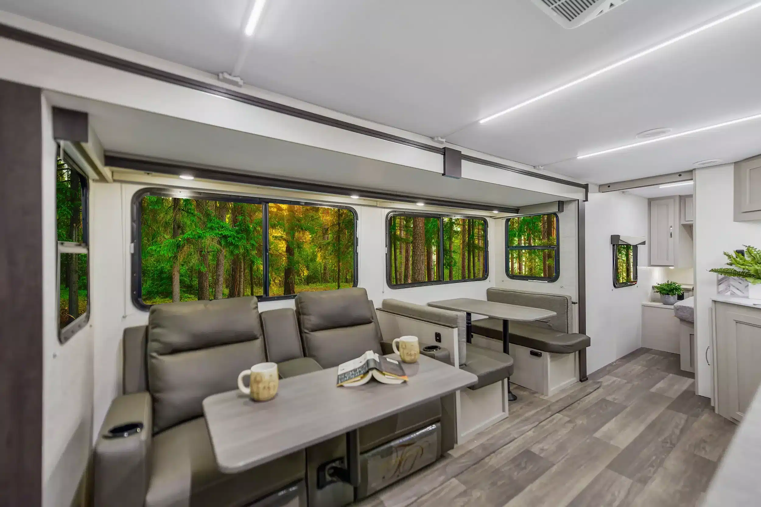 Moderner, heller Innenraum eines amerikanischen Shadow Cruiser 261RB Travel Trailer mit Sofa, Esstisch und Ausblick in den Wald