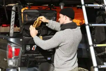 Mann nutzt iKamper Taschen-Organizer, der am Fahrzeug und neben einer Dachzelt-Leiter befestigt ist