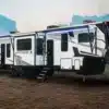 Der Sportster X Toy Hauler als Fifth-Wheel-Anhänger mit ausgefahrenen Markisen und geöffneter Einstiegstreppe auf einer Lichtung.