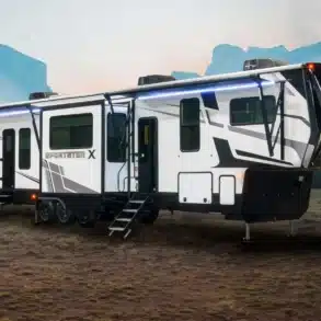 Der Sportster X Toy Hauler als Fifth-Wheel-Anhänger mit ausgefahrenen Markisen und geöffneter Einstiegstreppe auf einer Lichtung.