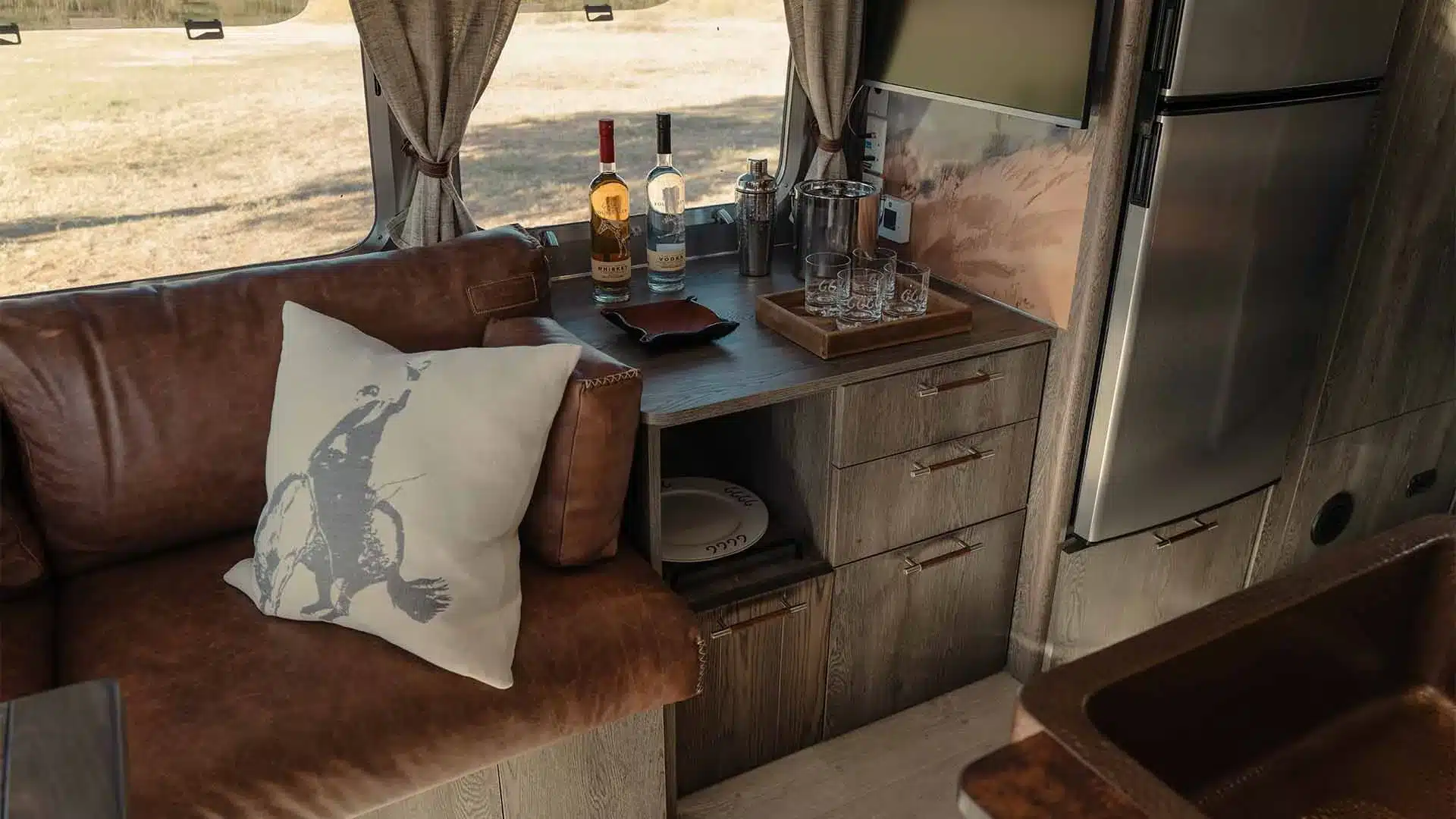 Detailaufnahme des Innenraums eines amerikanischen Travel Trailers mit brauner Ledercouch, Holzmöbeln, Kühlschrank und Barbereich