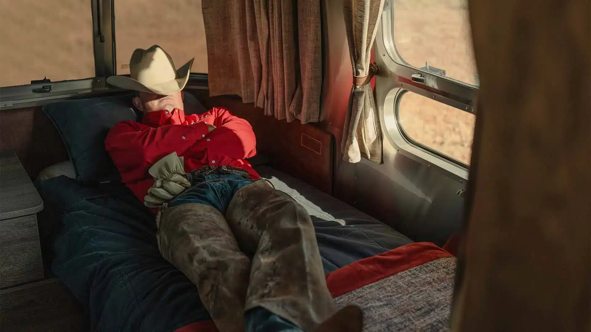 Cowboy entspannt auf dem Bett im Innenraum eines Stetson + 6666 Travel Trailers mit Western-Charme