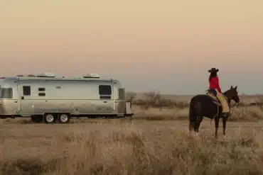 Stetson + 6666 Special Edition Travel Trailer mit Cowboy auf Pferd in weiter Prärie, Sonnenuntergang, Western-Stimmung