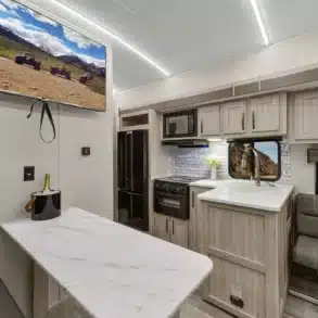 Innenraumfoto eines Stryker STG3413 Toyhaulers mit Küchenzeile, Sitzecke und Fernseher.