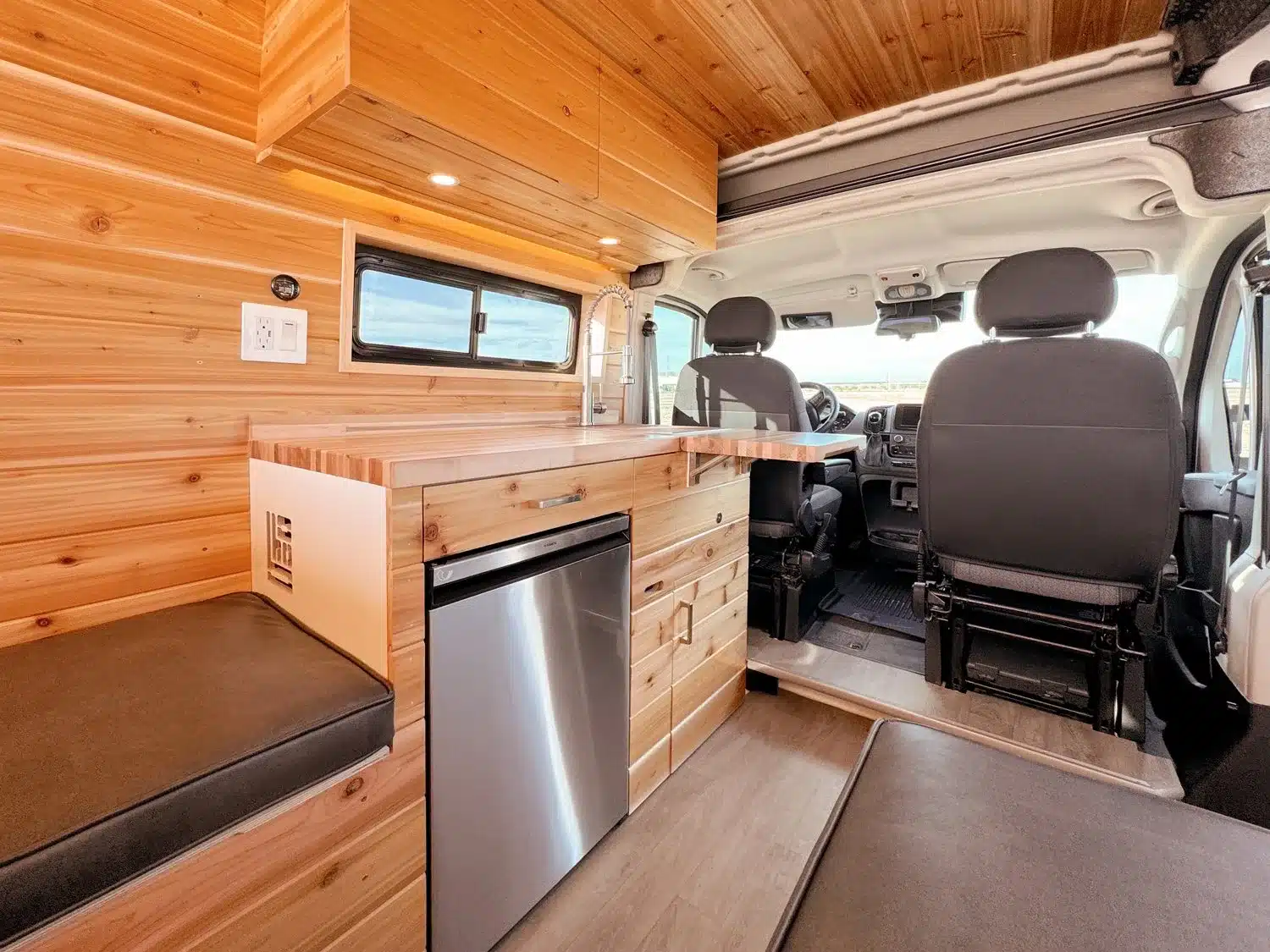 Innenansicht THE 505 RAM Promaster Camper Van mit Küchenzeile, Sitz- und Arbeitsbereich aus Holz und Fahrerhaus.