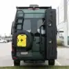 Heck von grünem Mercedes Sprinter Campervan mit Offroad-Trägermodulen, Reserverad, Außenleiter und großem Staubox-System