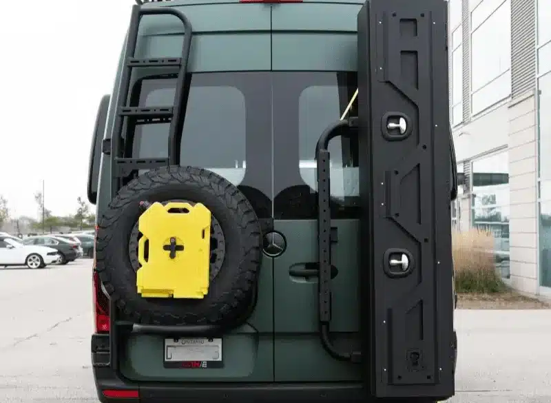 Heck von grünem Mercedes Sprinter Campervan mit Offroad-Trägermodulen, Reserverad, Außenleiter und großem Staubox-System