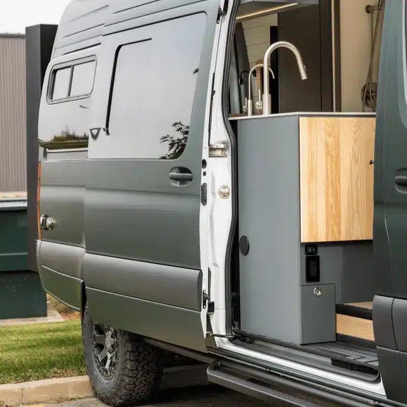 Ausgebauter Mercedes Sprinter Van mit geöffneter Tür und moderner Küchenzeile im Eingangsbereich