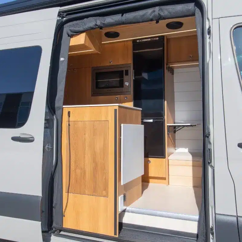 Blick in den Innenraum eines ausgebauten Mercedes Sprinter 170 Campervans mit Küchenelementen, Schränken und Sitzecke