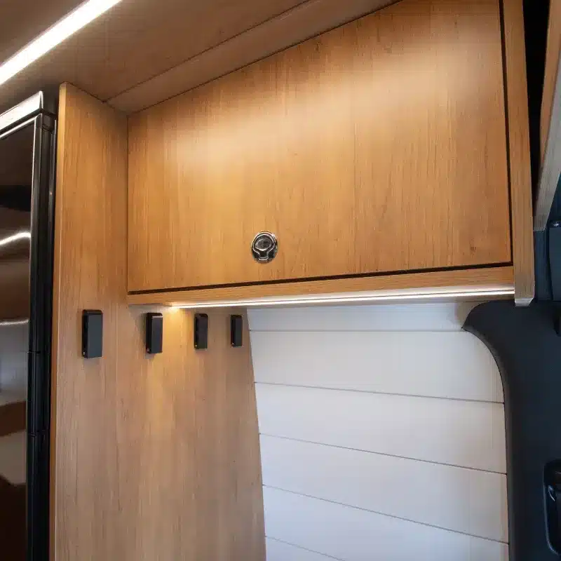 Oberschrank mit Holzdekor, Kleiderhaken und Seitenwand im Innenausbau des Mercedes Sprinter Campers.