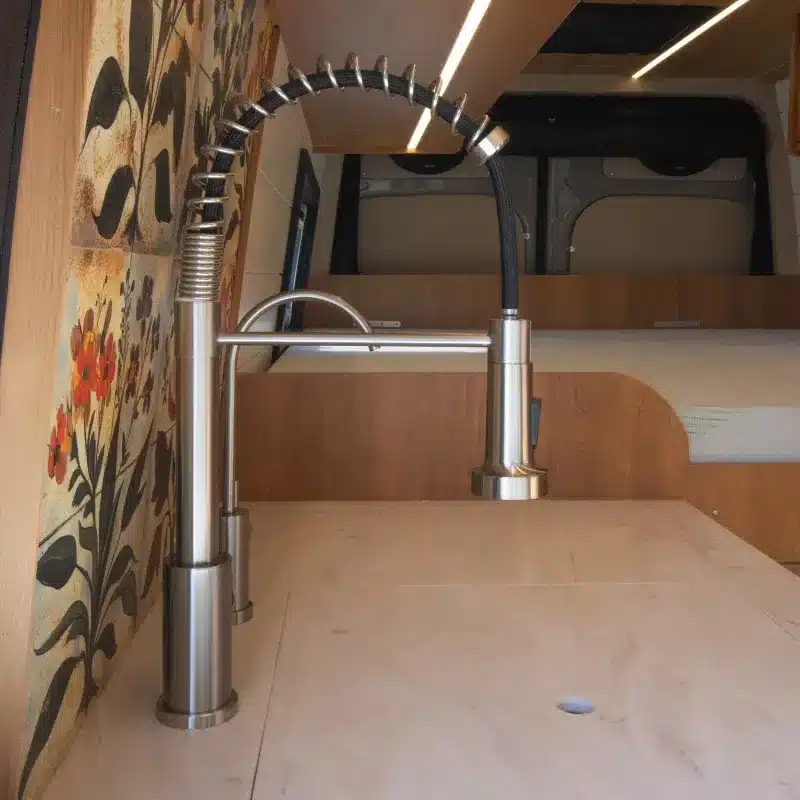 Edelstahl-Küchenarmatur und helle Arbeitsplatte in einem Campervan-Ausbau auf Basis des Mercedes Sprinter 170, mit floraler Wandverkleidung.