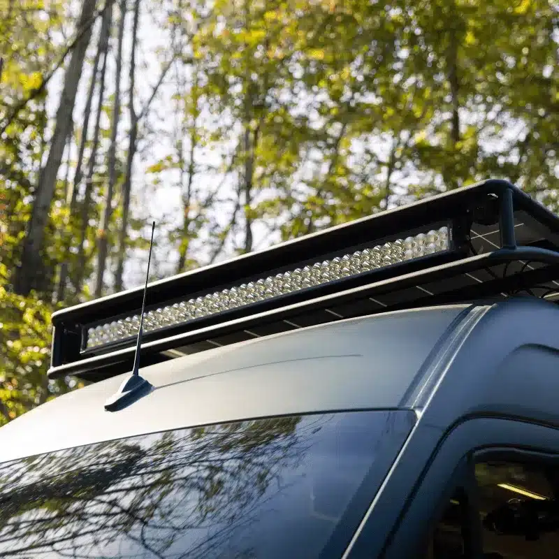 Dachträger mit montierter LED-Lightbar auf einem Mercedes Sprinter Camper, umgeben von Bäumen.